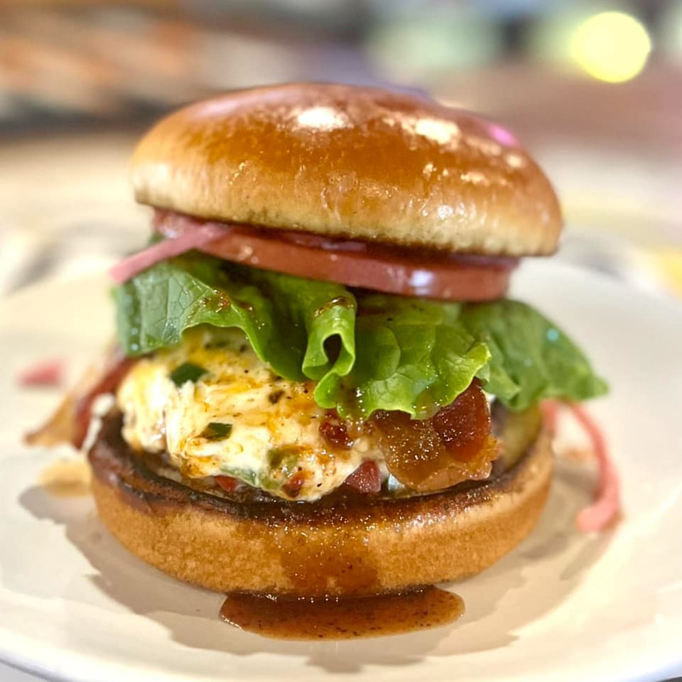 A Crooked Tale Gastropub burger with bacon, lettuce, tomato, and a creamy sauce on a toasted bun.
