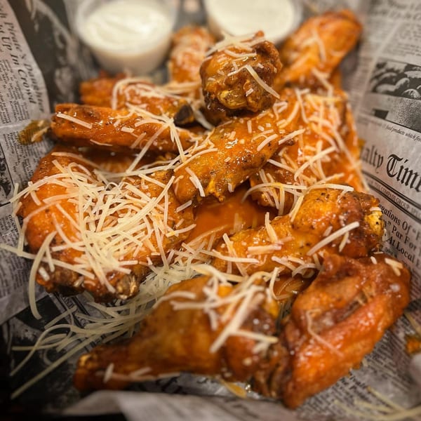 Crooked Tale Gastropub's chicken wings, coated in sauce and shredded cheese, served in a basket.