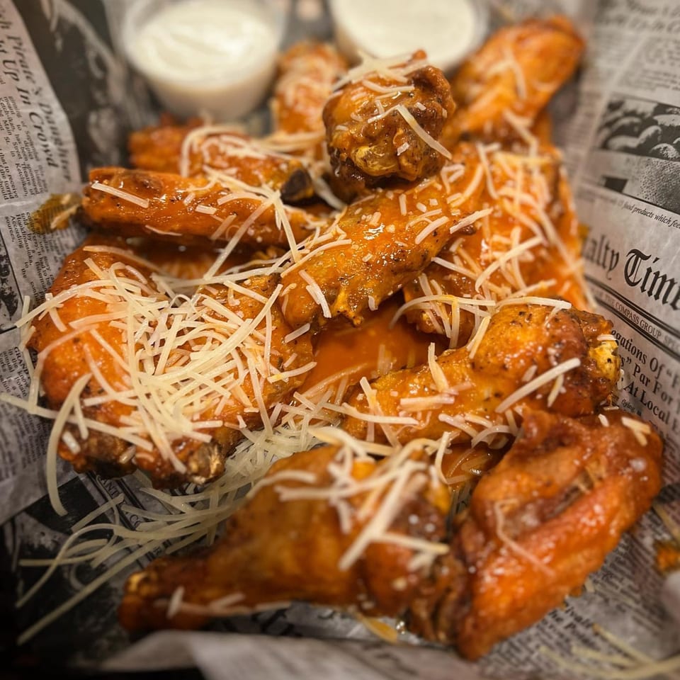 Crooked Tale Gastropub's chicken wings, coated in sauce and shredded cheese, served in a basket.