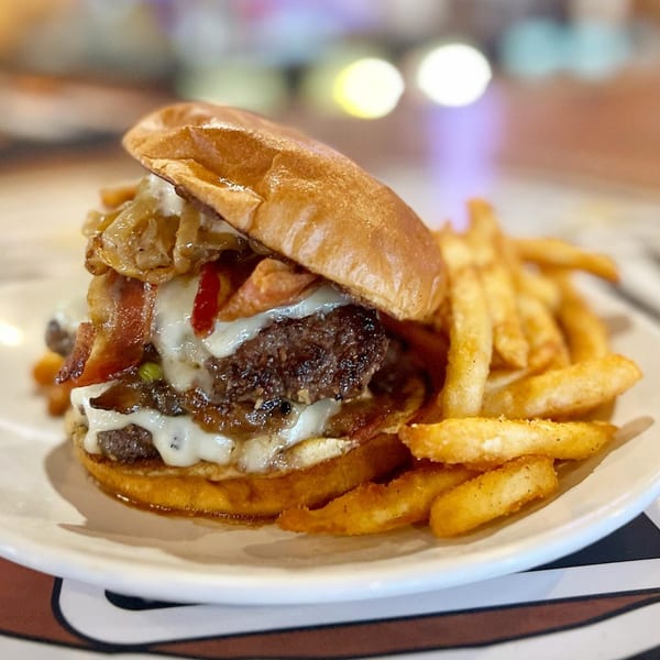 A Crooked Tale Gastropub burger with bacon, caramelized onions, and melted cheese, served with fries.