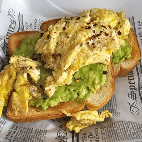 Scrambled eggs and avocado toast on newspaper-patterned paper at Crooked Tale Gastropub.