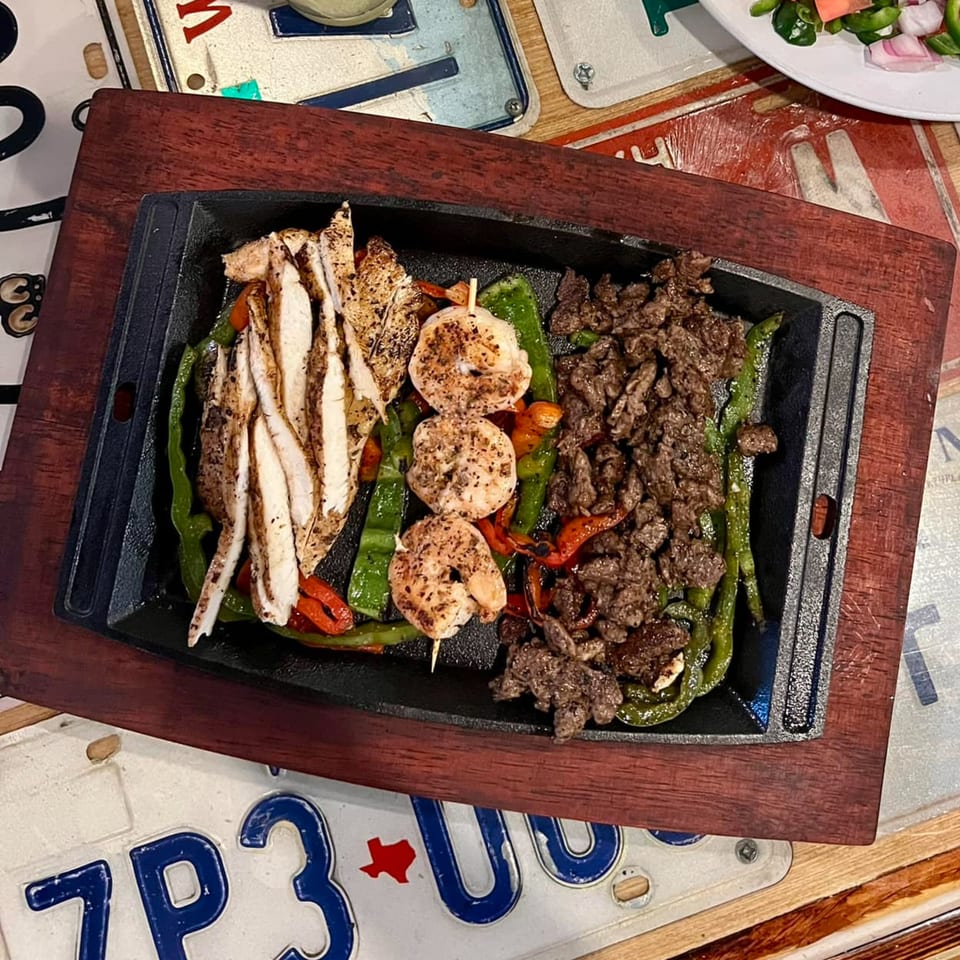 Sizzling fajitas with chicken, shrimp, and beef, bell peppers, and onions on a cast iron platter.