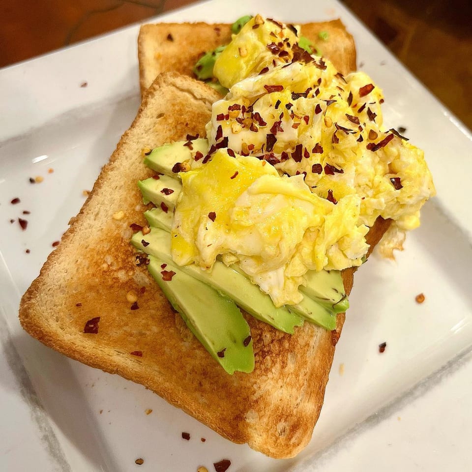 Avocado toast topped with scrambled eggs and red pepper flakes on a white plate.
